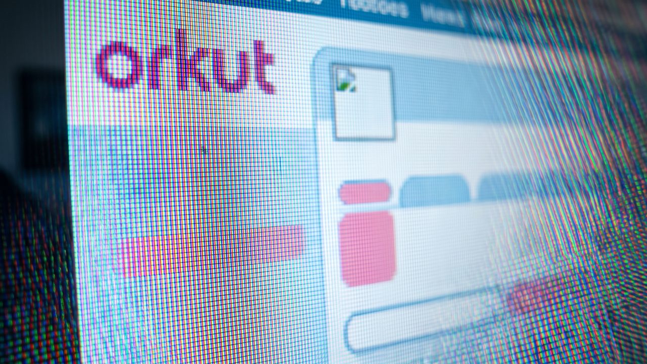 Fotografia macro da tela de um monitor LCD antigo tão próxima que os subpixels vermelho, verde e azul ficam visíveis, exibindo o logotipo em minúsculas 'orkut' e fragmentos da interface azul e rosa do site